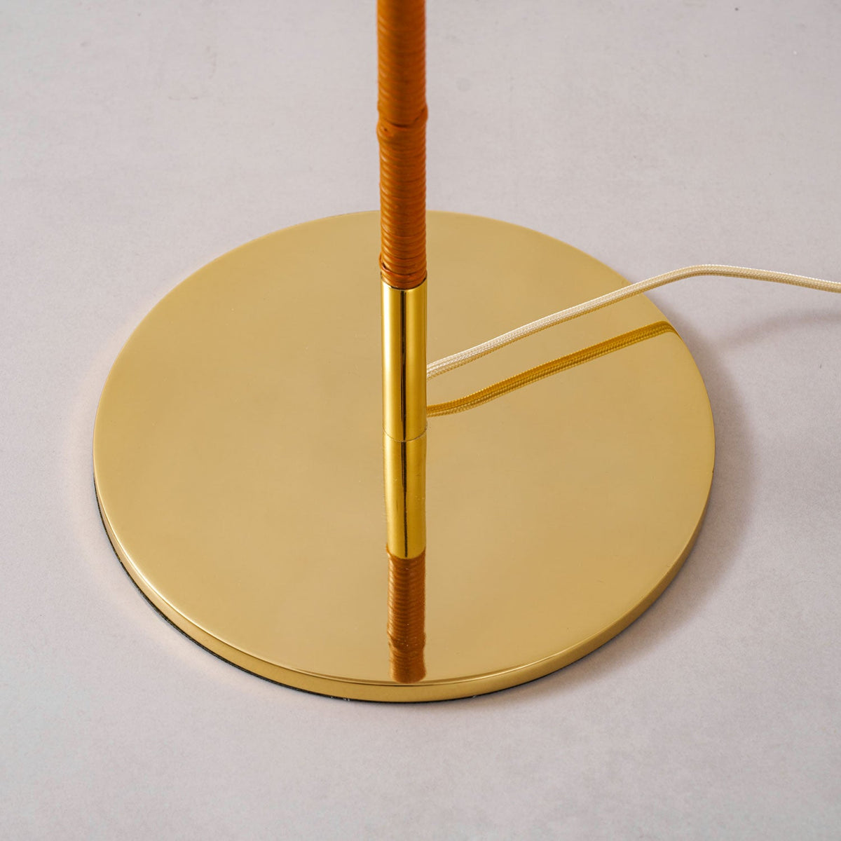 Close view of the round polished brass base of this Clérachic floor lamp, where the tan wrapped stem meets a brass collar.