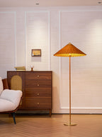 Lit Clérachic floor lamp with a woven rattan shade, beside a walnut chest of drawers with a cane door, on a herringbone floor.