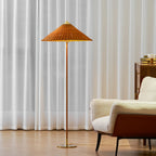 Clérachic floor lamp with a rattan shade in front of white sheer curtains, beside a cream armchair with a rust-brown back.