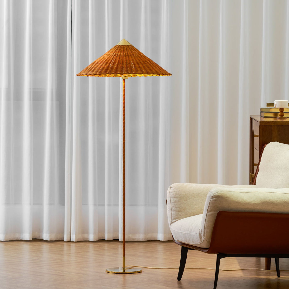 Clérachic floor lamp with a rattan shade in front of white sheer curtains, beside a cream armchair with a rust-brown back.