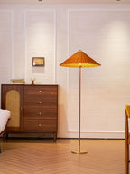 Shown here, a Clérachic floor lamp with a rattan shade casts a warm glow on a panelled wall, next to a walnut chest and a chair upholstered in mustard.