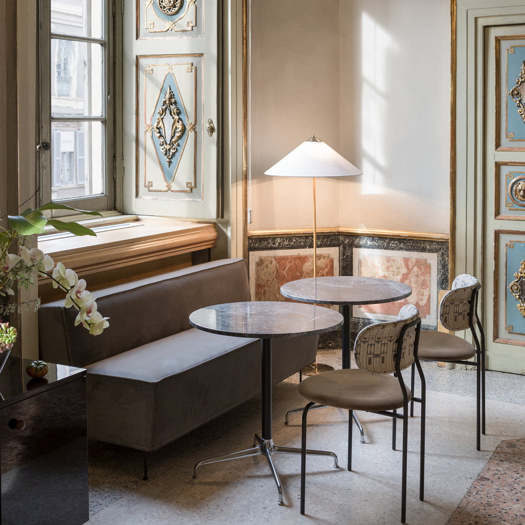 Pictured here, a Clérachic floor lamp with a white conical shade in a pale room with a round marble table, two café chairs and a window seat.