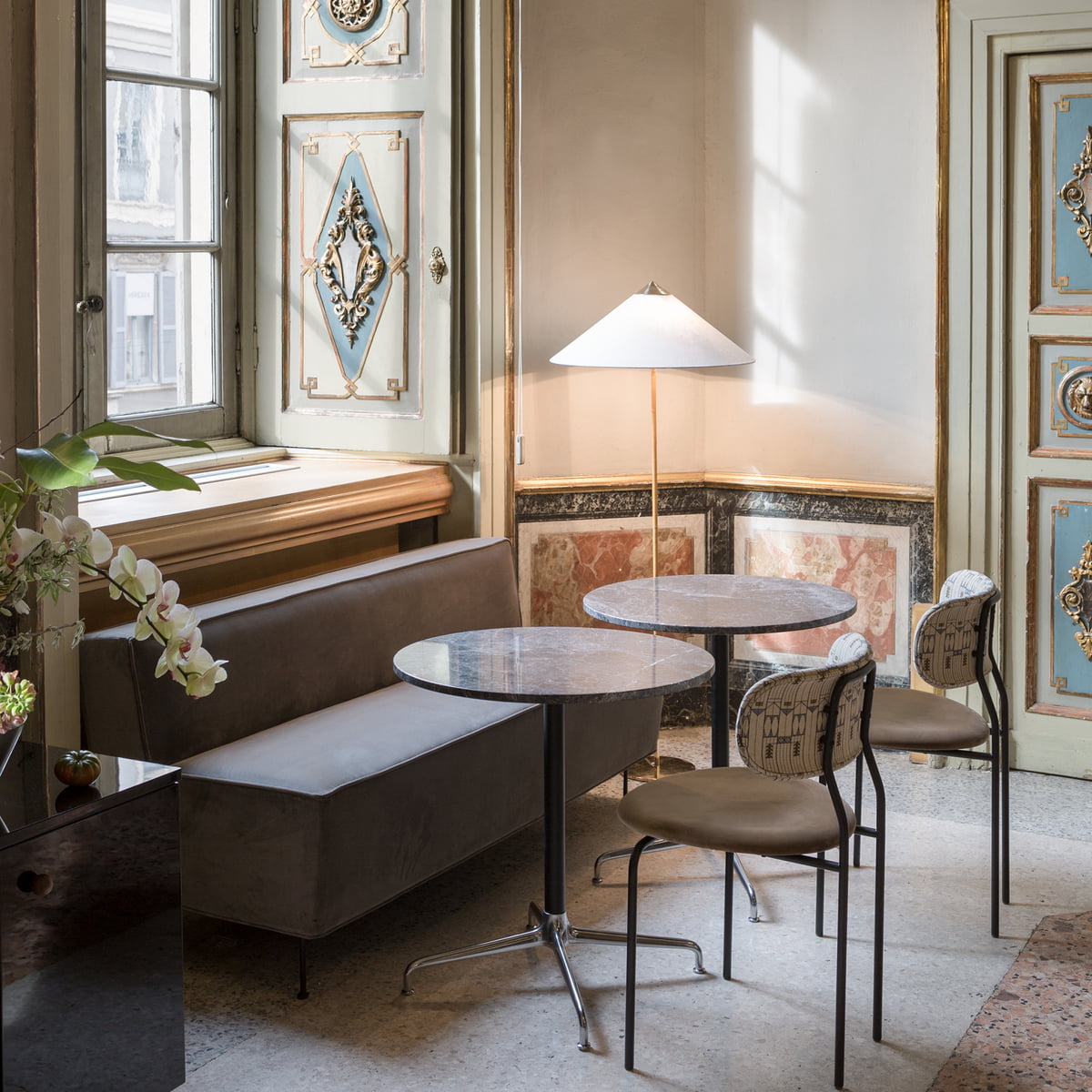 Pictured here, a Clérachic floor lamp with a white conical shade in a pale room with a round marble table, two café chairs and a window seat.
