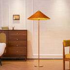 Full-length view of this Clérachic floor lamp with a rattan shade, in front of a walnut chest of drawers and a framed picture.