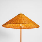 Clérachic floor lamp with a woven rattan shade and a brass cap, seen from below, showing the cane-wrapped stem and the brass fitting.