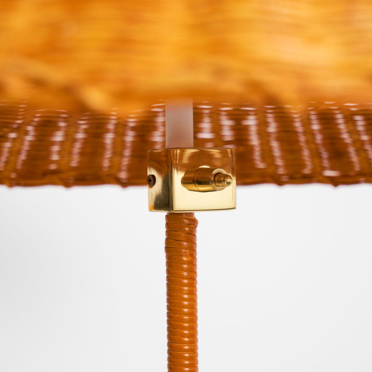 Close view of the brass fitting and the cane-wrapped stem beneath the woven shade on this Clérachic floor lamp.