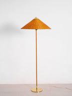 This Clérachic floor lamp with a rattan shade and a cane-wrapped stem stands on a brass base, shown against a light wall and floor.