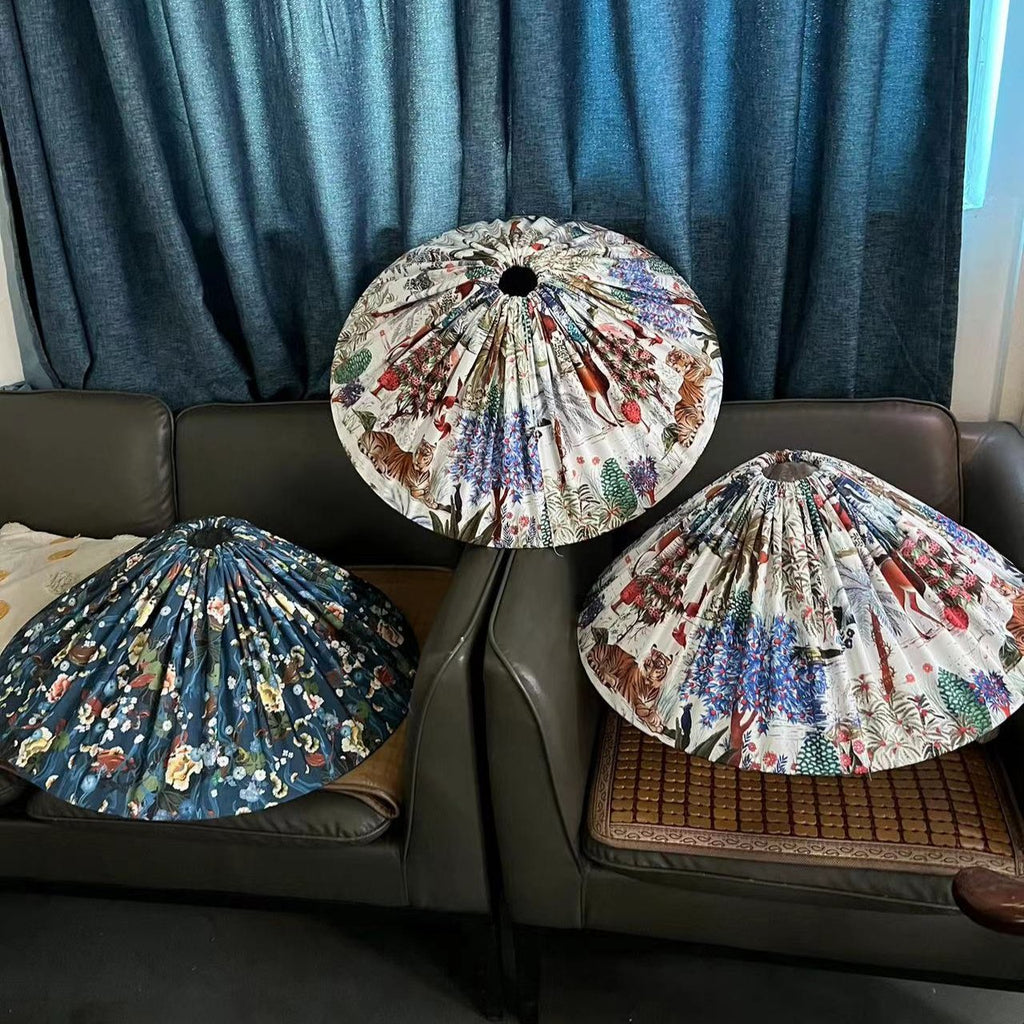 Three loose pleated conical lampshades in floral prints on a dark sofa, two of them blue and one white, for this Clérachic floor lamp.
