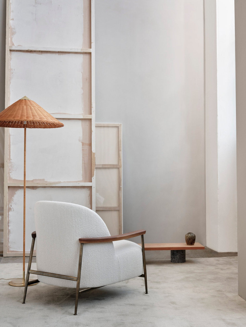 Clérachic floor lamp with a woven rattan shade by a white boucle armchair and a wooden bench, against a pale studio wall.