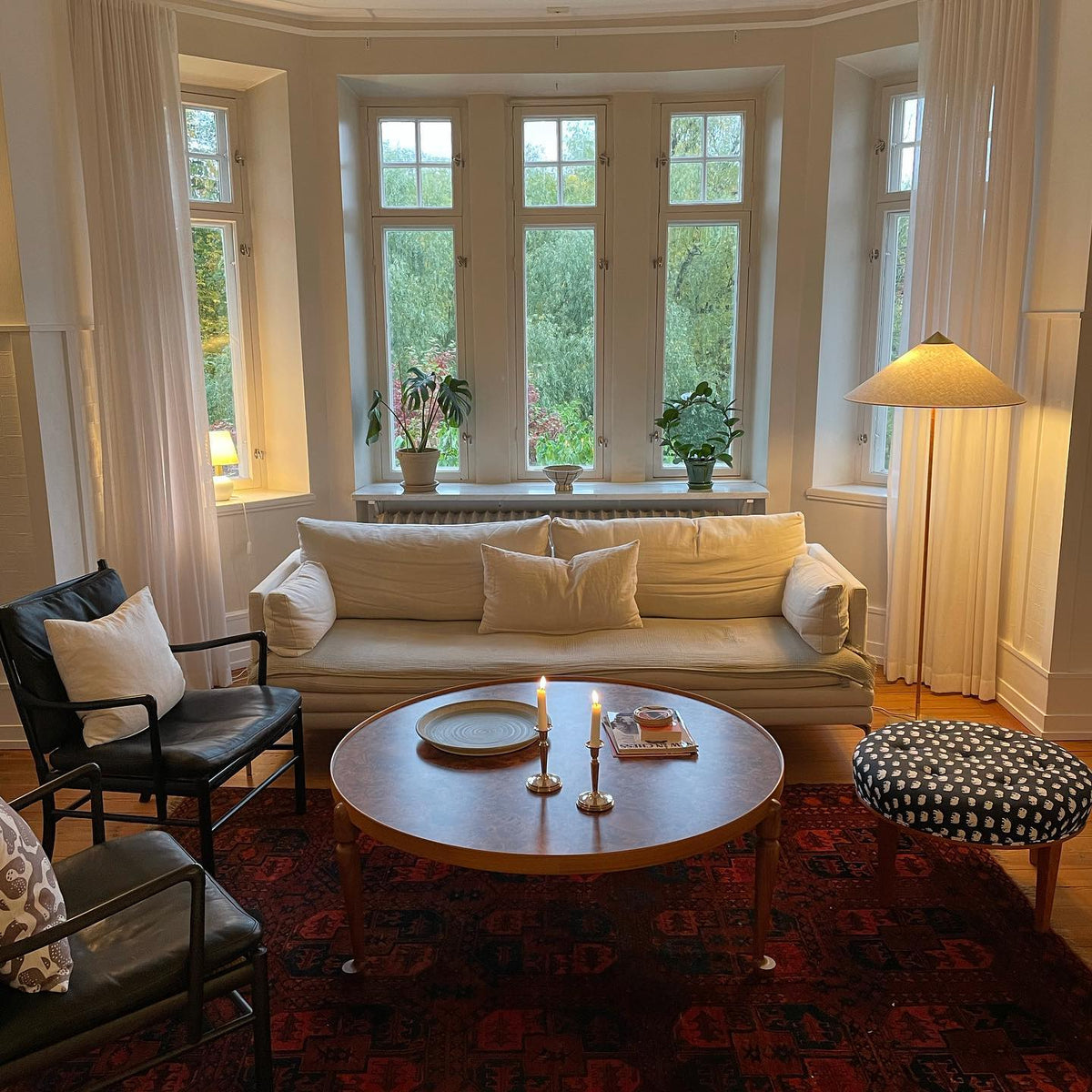 Clérachic floor lamp with a white conical shade in a bay-windowed sitting room, behind a cream sofa and a round wooden coffee table.