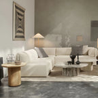 A Clérachic floor lamp with a small white shade in a living room with a cream modular sofa, a stone coffee table and a patterned wall hanging.