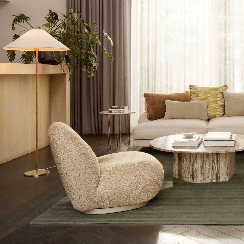 Clérachic floor lamp with a white conical shade beside a speckled rounded armchair, in a room with a stone round coffee table and a green rug.