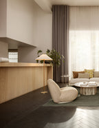 In this photo, a Clérachic floor lamp with a warm-toned shade stands beside a boucle armchair and a wood counter, in a room with a dark herringbone floor.