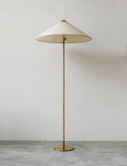 This Clérachic floor lamp with a pale textured shade and a rattan-wrapped stem stands against a grey wall on a concrete floor.