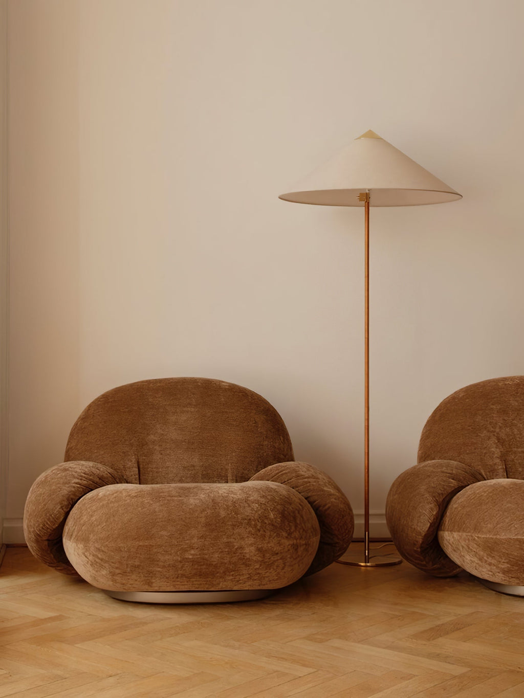Pictured here, a Clérachic floor lamp with a cream shade stands between two rounded brown velvet armchairs on a light wood floor.