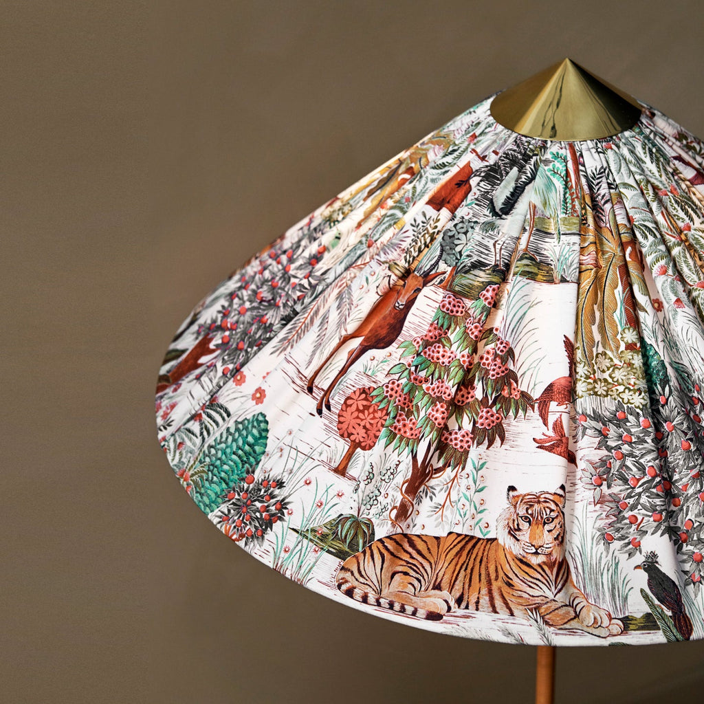 Angled view of this Clérachic floor lamp's pleated shade printed with a tiger and trees, with a brass top cap, against a taupe wall.