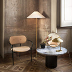 This Clérachic floor lamp with a white conical shade stands in a panelled room, beside a cane-backed chair and a round marble table.