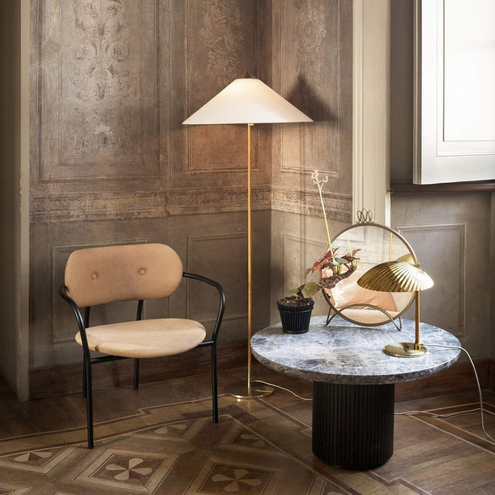 This Clérachic floor lamp with a white conical shade stands in a panelled room, beside a cane-backed chair and a round marble table.
