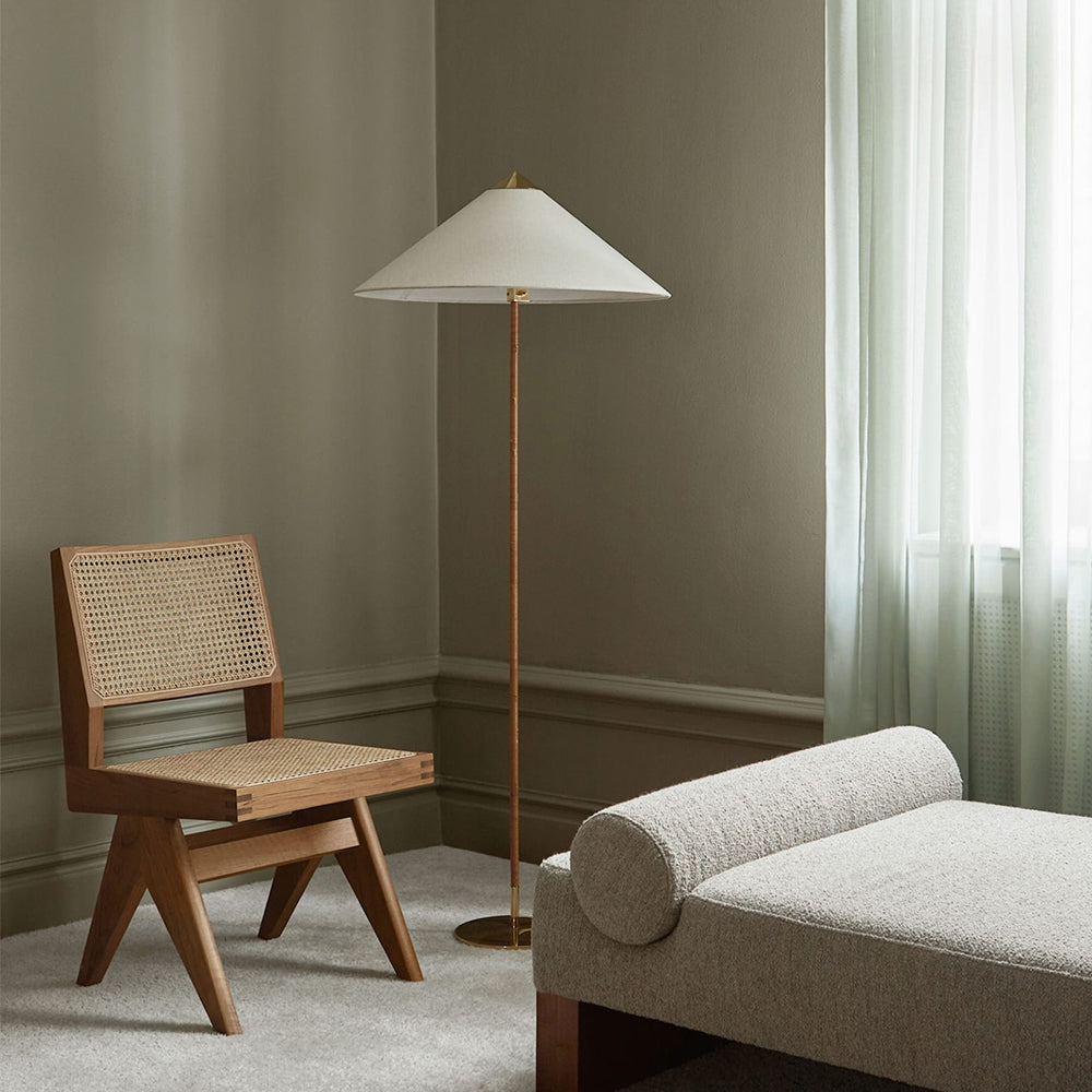 Clérachic floor lamp with a white conical shade in a muted green room, beside a cane-backed wooden chair and a cushioned daybed.