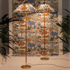 Two Clérachic floor lamps with printed tiger-and-tree shades stand in front of a wall hung with matching fabric, beside plants.
