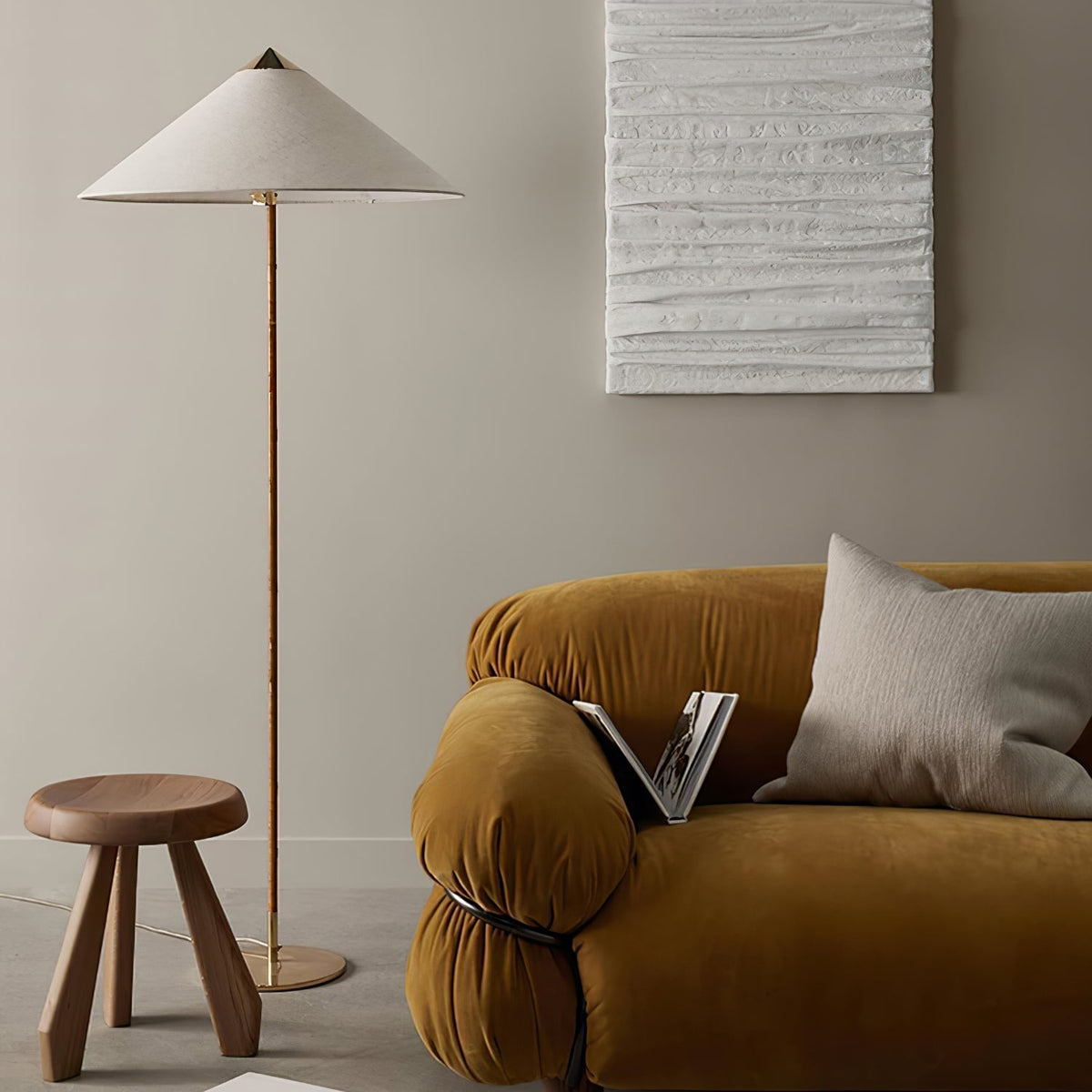 This Clérachic floor lamp with a white shade stands beside a mustard velvet sofa, near a wooden stool and a textured white wall panel.