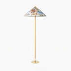 Clérachic floor lamp with a bright floral printed shade, a cane-wrapped stem and a brass base, on a white backdrop.