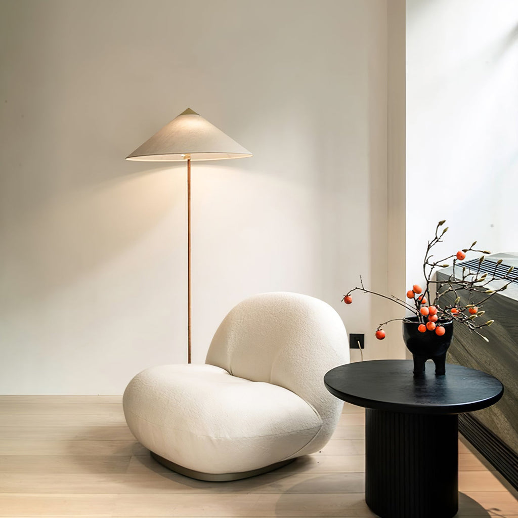 Clérachic floor lamp with a pale shade standing by a white boucle armchair and a round black side table, with a berry branch in a vase.
