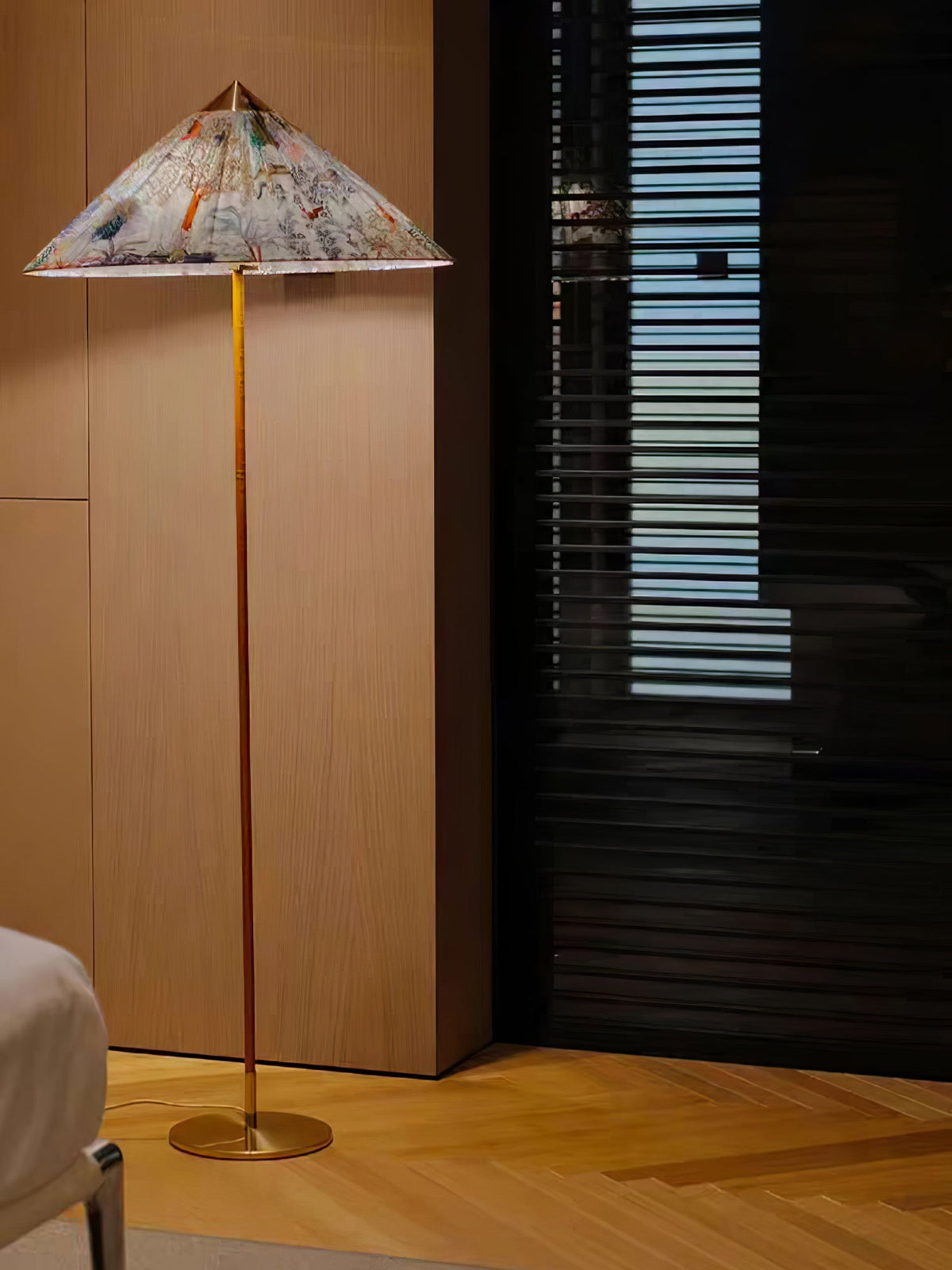A Clérachic floor lamp with a printed conical shade stands beside a wood-panelled wall and a dark slatted screen, on a herringbone floor.