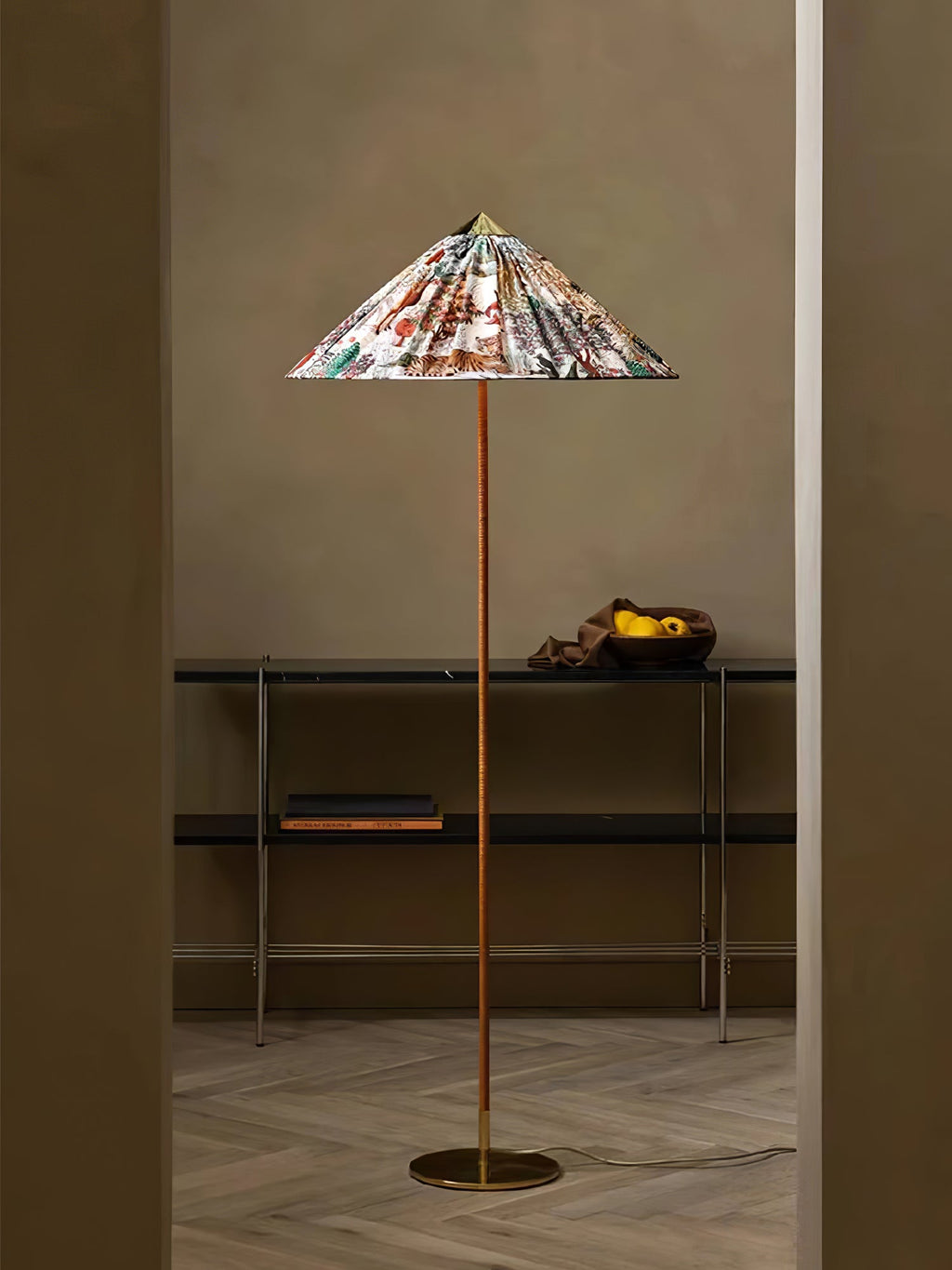 This Clérachic floor lamp with a printed floral shade stands in a doorway above a console with a bowl of fruit, on a pale herringbone floor.