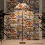 Pictured here, a Clérachic floor lamp with a printed shade of trees and animals stands in front of a matching fabric wall hanging, with plants either side.