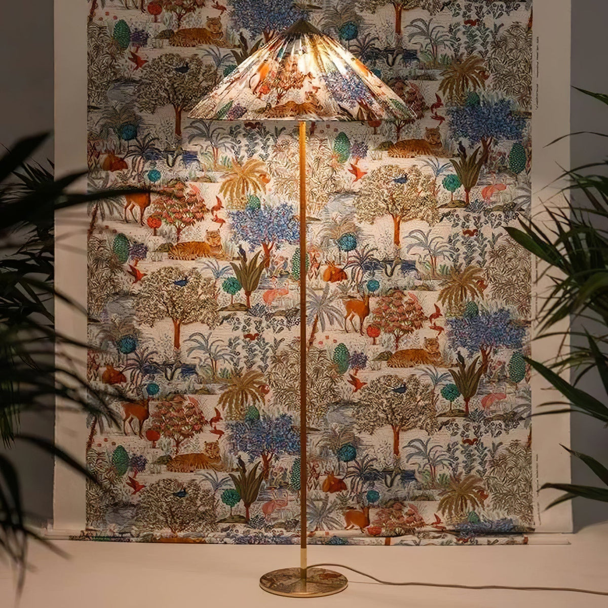Pictured here, a Clérachic floor lamp with a printed shade of trees and animals stands in front of a matching fabric wall hanging, with plants either side.