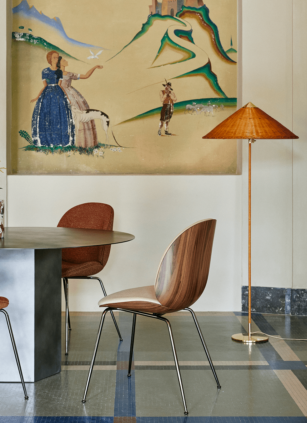 Clérachic floor lamp with a woven rattan shade above a round table, with two curved wood chairs and a painted mural behind.