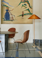 Clérachic floor lamp with a woven rattan shade above a round table, with two curved wood chairs and a painted mural behind.