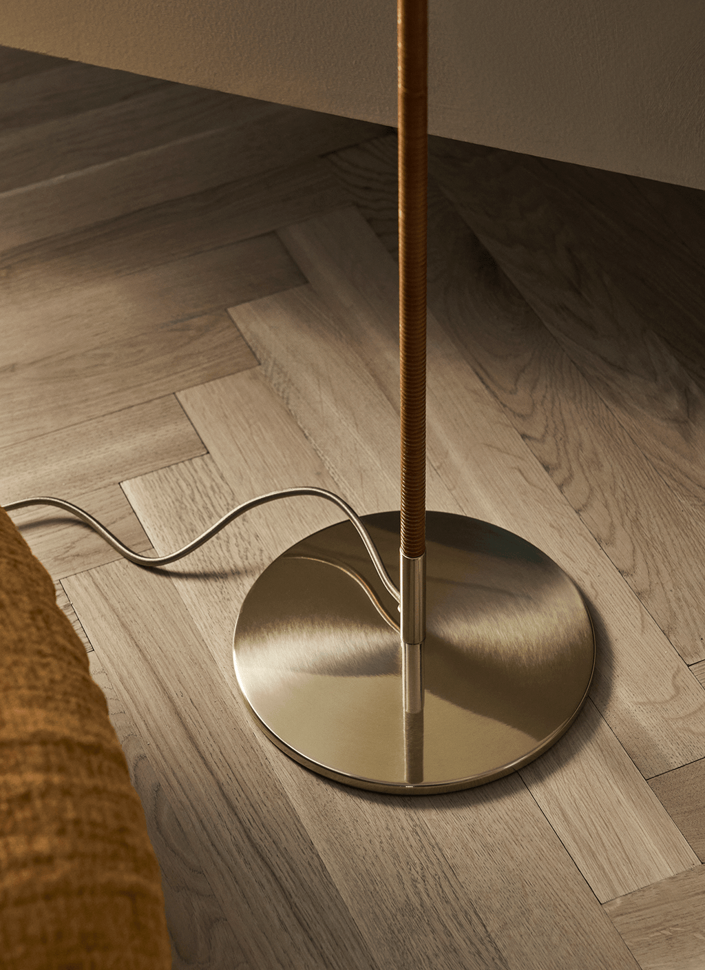 Close view of the dark brown cane wrap on the stem and the round brushed brass base of this Clérachic floor lamp, on a wood floor.