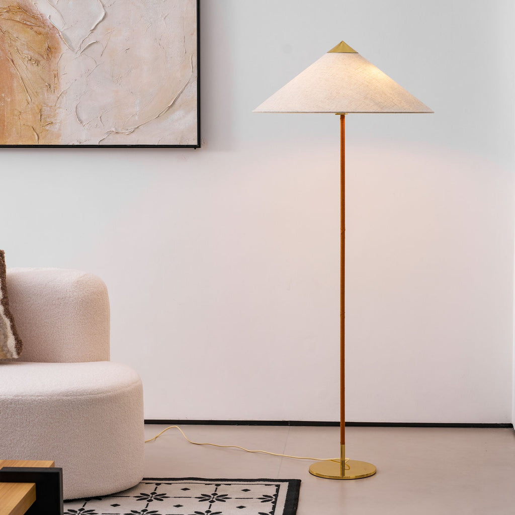 This Clérachic floor lamp with a natural linen-look shade and a tan leather-wrapped stem stands in front of a framed abstract painting.