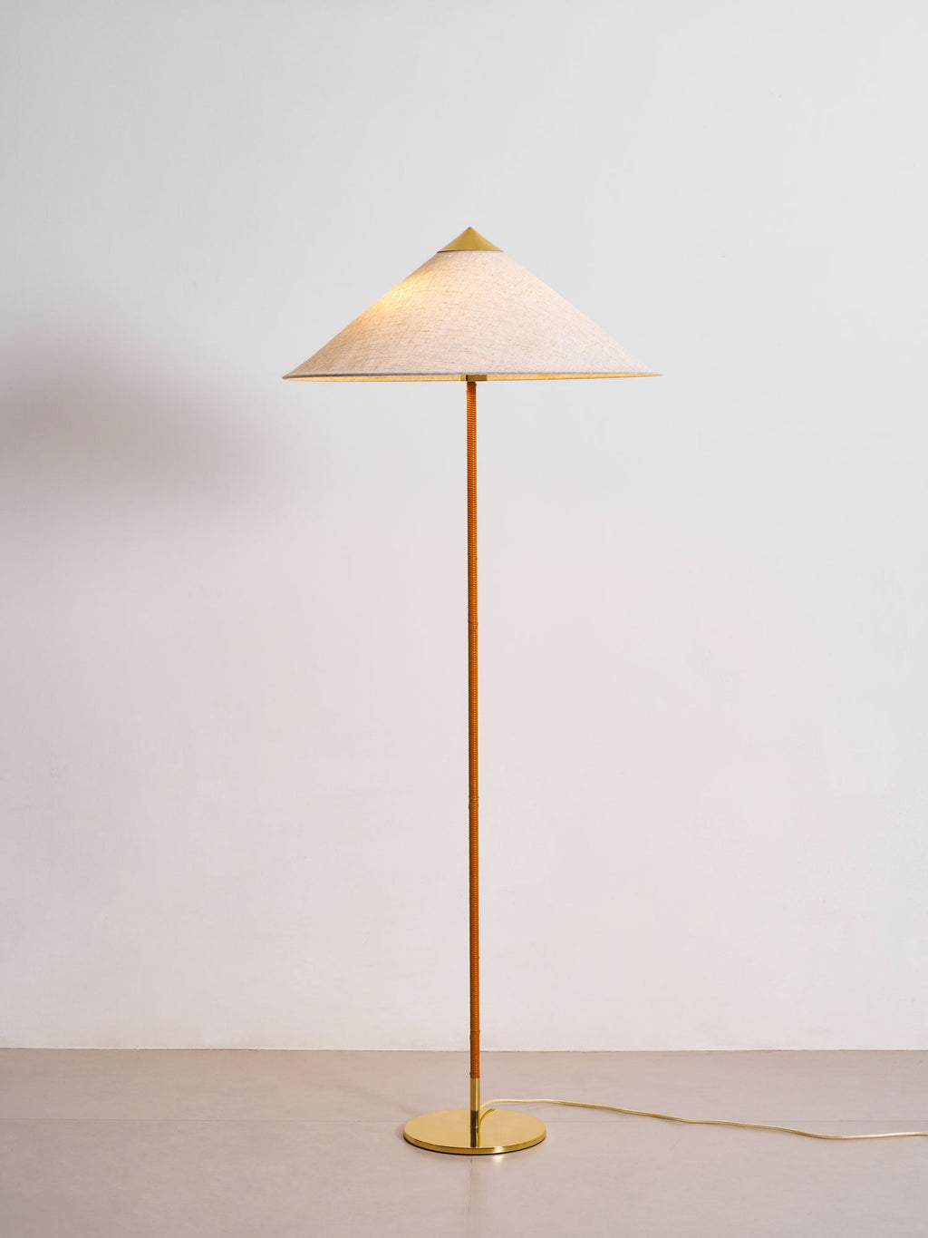 This Clérachic floor lamp with a linen-look shade and a polished brass cap stands on a pale floor against a light grey wall.