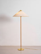 This Clérachic floor lamp with a linen-look shade and a polished brass cap stands on a pale floor against a light grey wall.