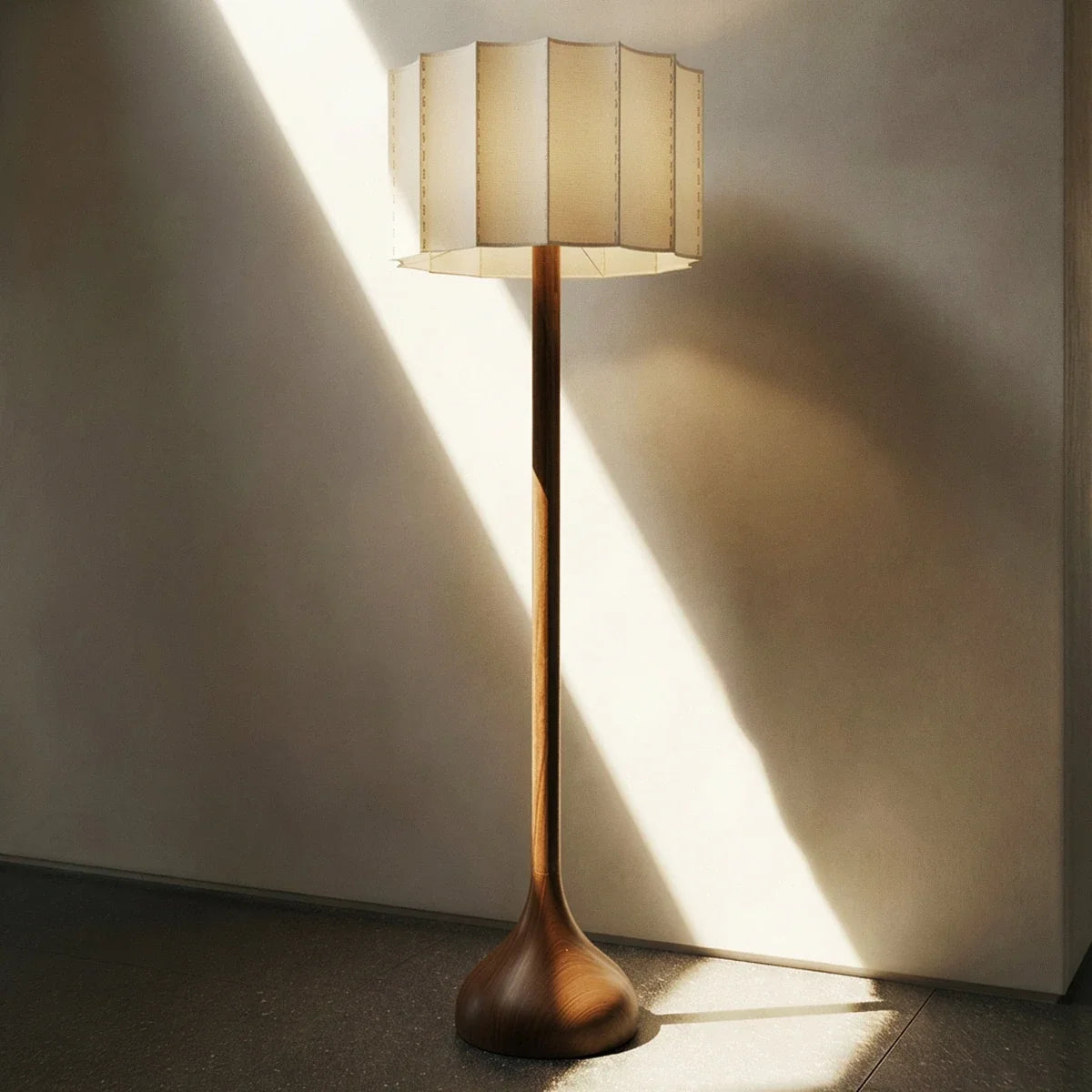 Clérachic floor lamp with wooden base and pleated shade standing in a sunbeam against a plaster wall.