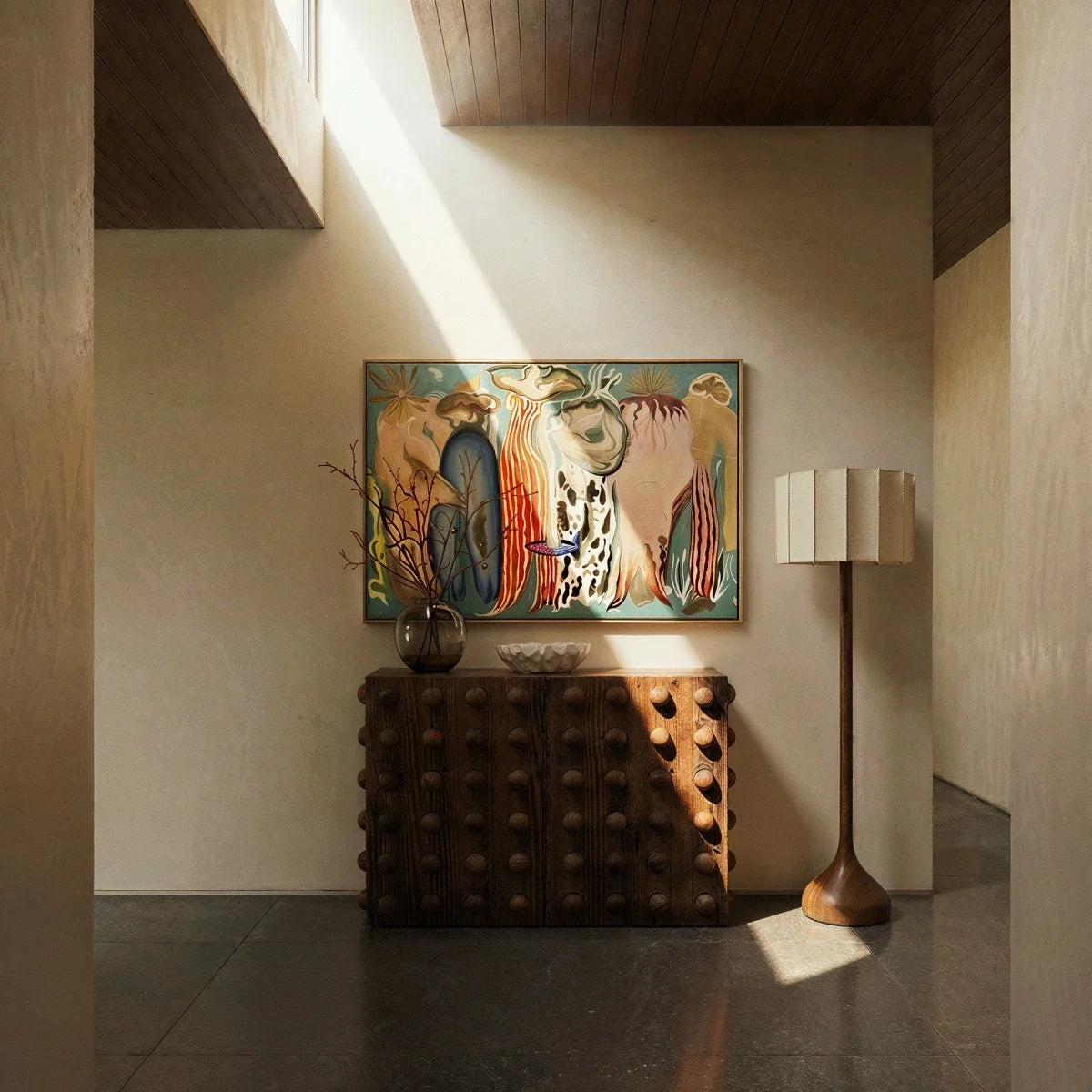 Clérachic floor lamp beside a studded wooden console and large framed painting in a calm hallway with a stone floor.