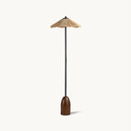 Floor lamp from Clérachic with a wavy-edged raffia shade, a slim black stem and a rounded walnut base, on a plain white backdrop.