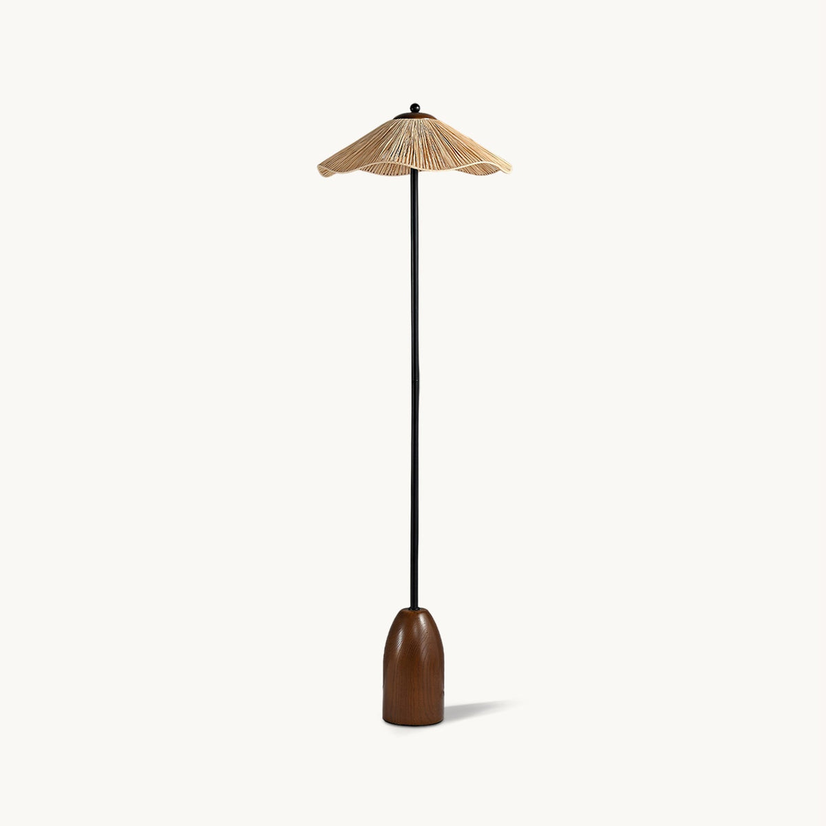 Floor lamp from Clérachic with a wavy-edged raffia shade, a slim black stem and a rounded walnut base, on a plain white backdrop.