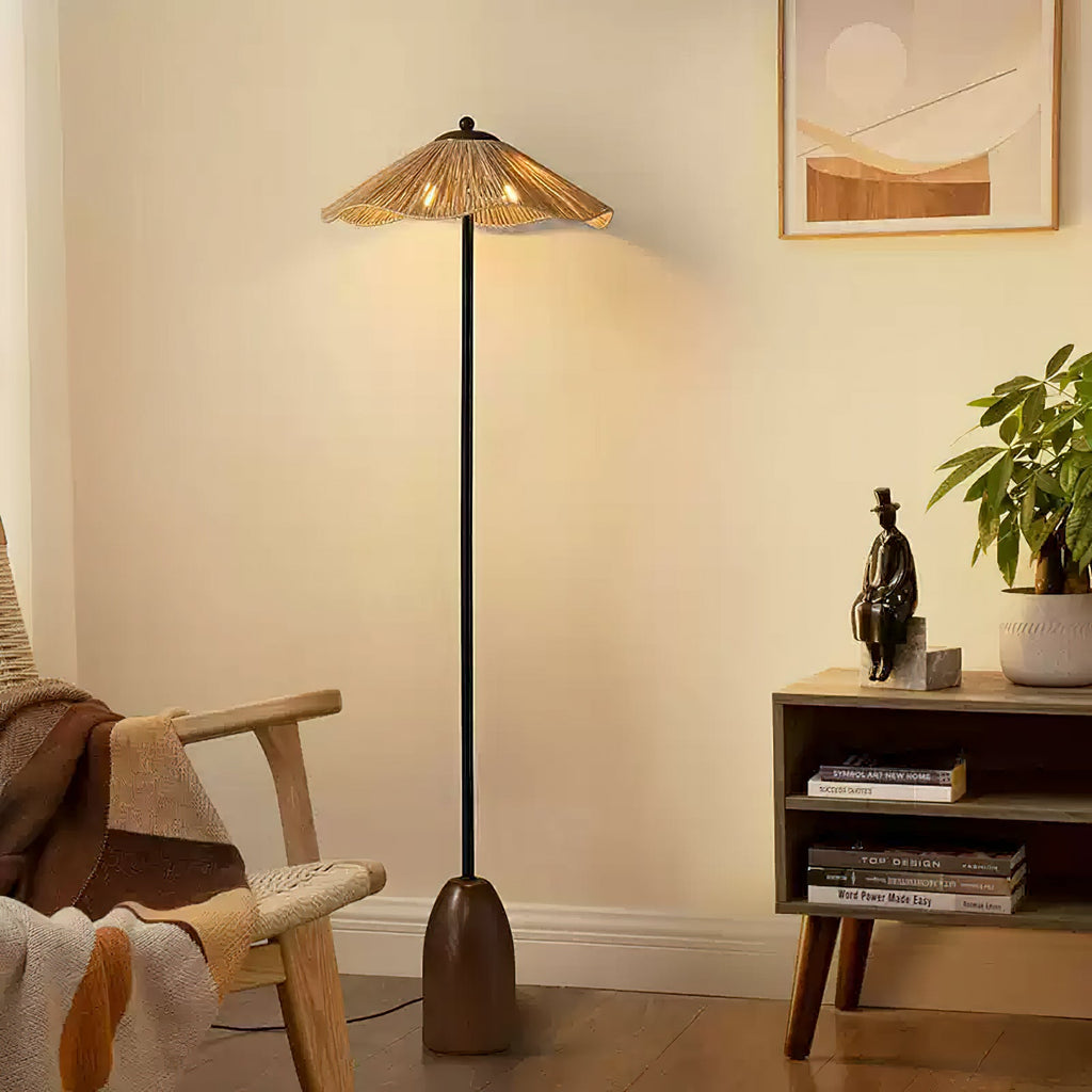 Warm light spills from the raffia shade of this Clérachic floor lamp onto a cream wall, beside a rattan chair and a small shelf.