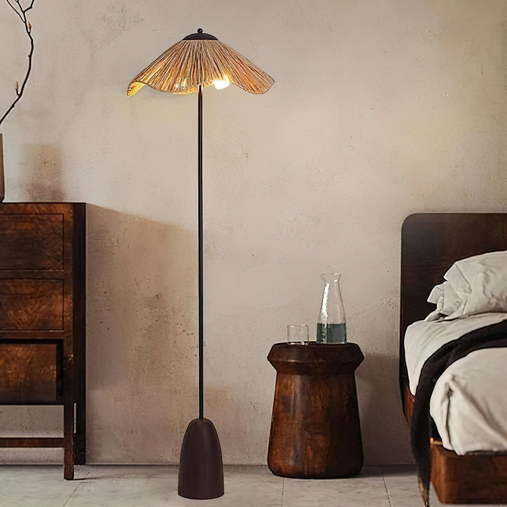 A Clérachic floor lamp with a raffia shade lights a corner with a carved wooden stool, a dark bed and a walnut cabinet.
