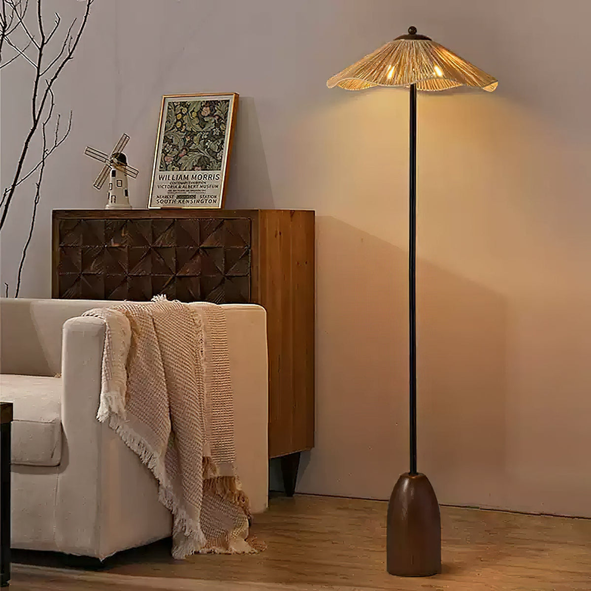 The raffia-shade Clérachic floor lamp stands behind a cream sofa with a fringed throw, in front of a carved wooden sideboard.
