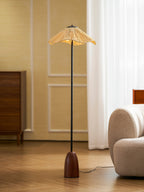 Clérachic floor lamp with a walnut base and a raffia shade, on a wooden floor beside a cream rounded sofa.