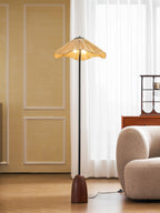 Closer view of the lit raffia shade and slim stem of this Clérachic floor lamp, with a cream sofa and sheer curtains behind.