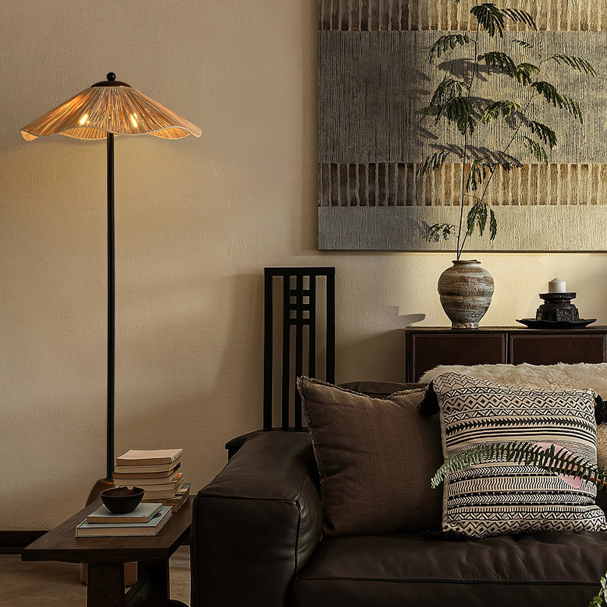A lit Clérachic floor lamp stands beside a leather sofa with woven cushions, below a large artwork and a potted tree.