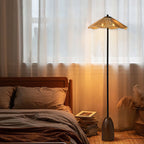 In a bedroom with sheer curtains and brown linen, the raffia shade of this Clérachic floor lamp glows amber.
