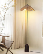 A Clérachic raffia-shade floor lamp beside long cream curtains and a woven chair, a tall branch in a vase behind it.