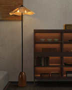 The lit raffia shade of this Clérachic floor lamp stands near a dark wooden shelving unit with bowls and books.